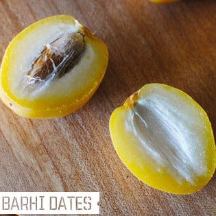 Two halves of a Barhi date on a wooden surface with 'Barhi Dates' text.