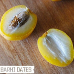 Two halves of a Barhi date on a wooden surface with 'Barhi Dates' text.